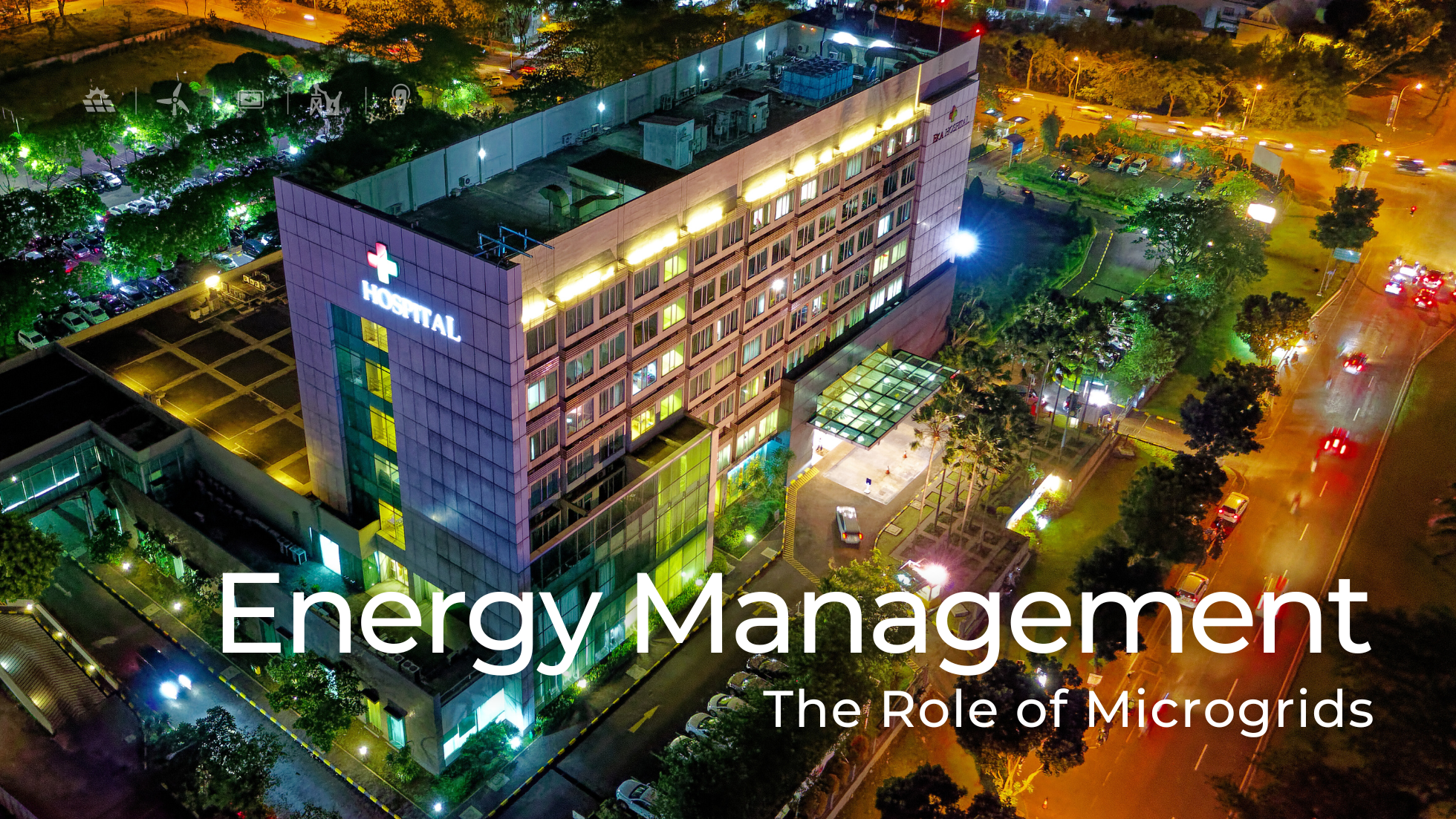 An aerial view of a well-lit hospital building at night surrounded by trees and parking spaces. Streetlights and cars with headlights create a vibrant, urban atmosphere. A caption overlay reads 'Energy Management: The Role of Microgrids,' highlighting the topic of energy solutions.