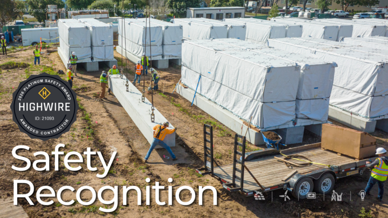 Aerial view of a battery energy storage site under construction, with workers in safety gear installing large equipment units and a crane lifting a concrete pad. Overlay highlights Highwire Platinum Safety Award 2026 and “Safety Recognition.”